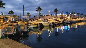 A marina with boats docked, palm trees, and a building with illuminated signage. - Quiet garden-level apartment with sea view (Sainte-Maxime)