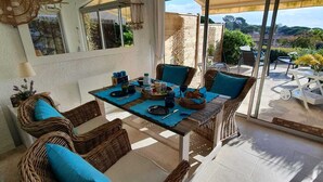 A dining area with wicker furniture and a table set for a meal. - Quiet garden-level apartment with sea view (Sainte-Maxime)