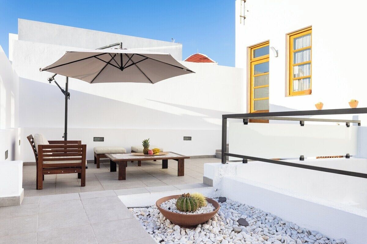 Une terrasse avec un banc en bois, une table garnie de fruits et un cactus dans un pot.