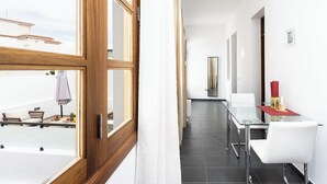 Una stanza moderna e luminosa con un tavolo in vetro e sedie bianche, una finestra con cornice in legno e vista su una terrazza con mobili da esterno.