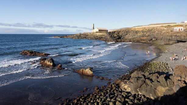 Una spiaggia rocciosa con onde, un faro e un edificio sulla riva.