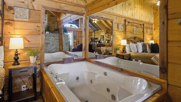 Een houten cabin met een grote spiegel, een ligbad voor twee personen, een klein tafeltje met een lamp en een knus zitgedeelte.