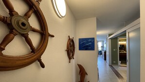 A hallway with nautical-themed wall decor, including a large wooden ship wheel and a smaller wheel, leading to a room with a view of the sea.