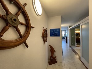 A hallway with nautical-themed wall decor, including a large wooden ship wheel and a smaller wheel, leading to a room with a view of the sea.