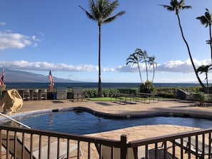 A pool area with a view of the ocean, outdoor seating, and palm trees.