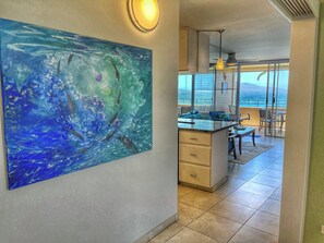 Een moderne keuken met een groot schilderij van dolfijnen, een eethoek met uitzicht op de oceaan en een balkon met terrasmeubels.
