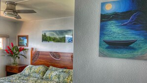 A bedroom with a bed, a ceiling fan, a night sky painting, and a framed landscape picture.