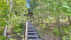 A wooden staircase leading up a forested hill with a rustic cabin in the background. - Peace on the Lake...close to Downtown Charlevoix (Charlevoix)