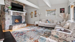 A cozy living room with a stone fireplace, a flat-screen TV, a white sofa, and a colorful rug. - Peace on the Lake...close to Downtown Charlevoix (Charlevoix)