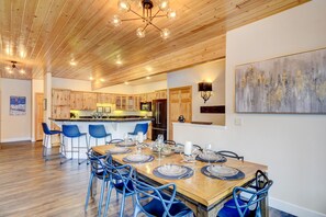Une cuisine moderne avec des meubles en bois, un îlot central doté de tabourets de bar et un coin repas avec une table en bois pouvant accueillir six personnes.