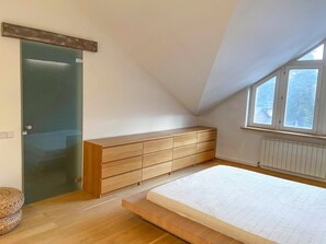 Un dormitorio con un aparador de madera, un vidrio, una cama con colchón y una ventana con vistas.