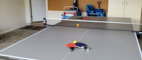 Een tafeltennistafel met twee batjes en een bal, een houten wand met sportattributen, en een deur op de achtergrond.