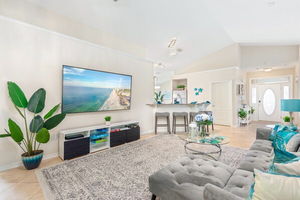 Uma sala de estar moderna com uma TV grande, assentos confortáveis, uma área de cozinha e um espaço para refeições.