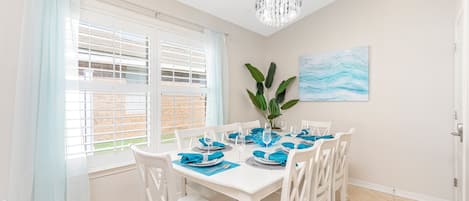A dining area with a white table set for four, blue napkins, and a plant on the table.