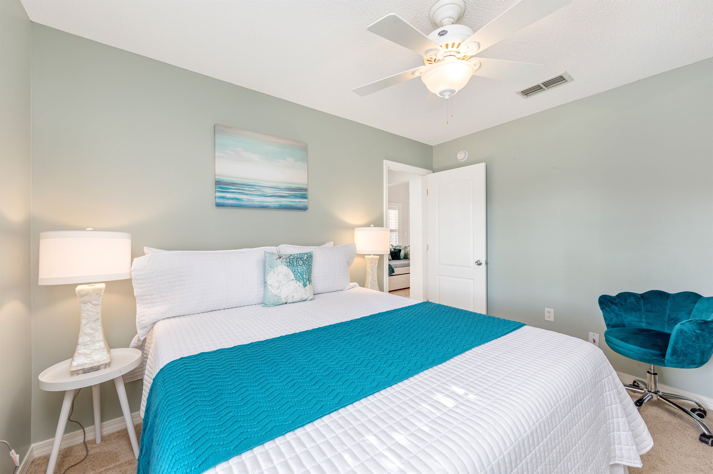 A bedroom with a bed, a ceiling fan, a nightstand, a lamp, a chair, and a door.