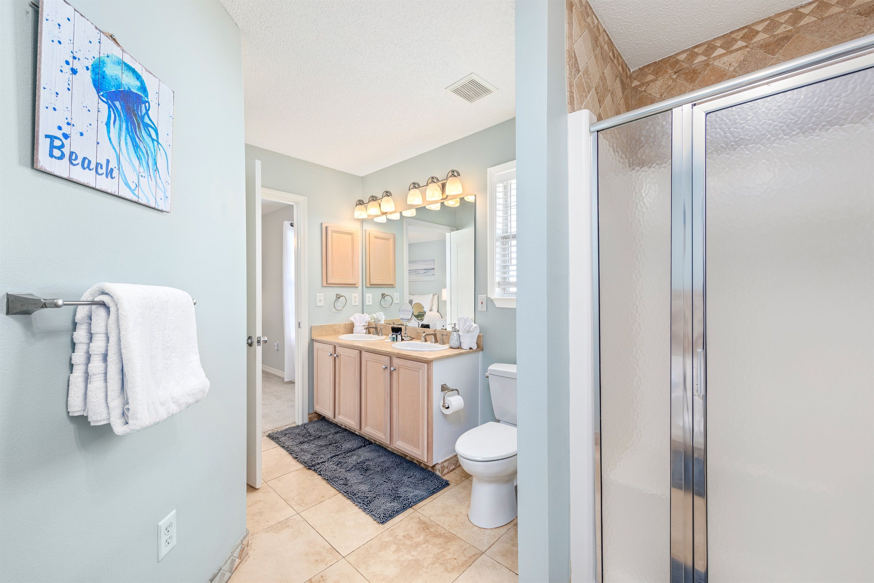 A bathroom with a light blue wall, a white toilet, a sink with a mirror above it, and a shower area.
