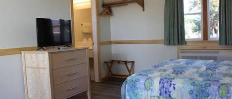 A bedroom with a bed, a dresser, a television, and a window with curtains.