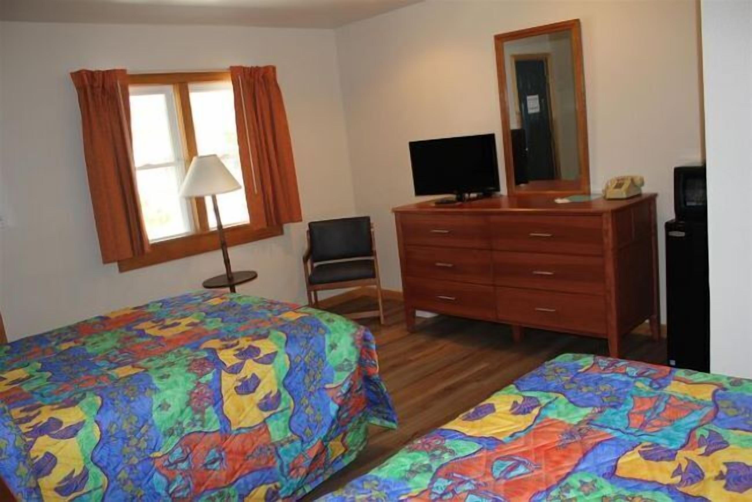 Habitación de hotel con dos camas, un escritorio, una silla, un aparador, un televisor y un espejo.