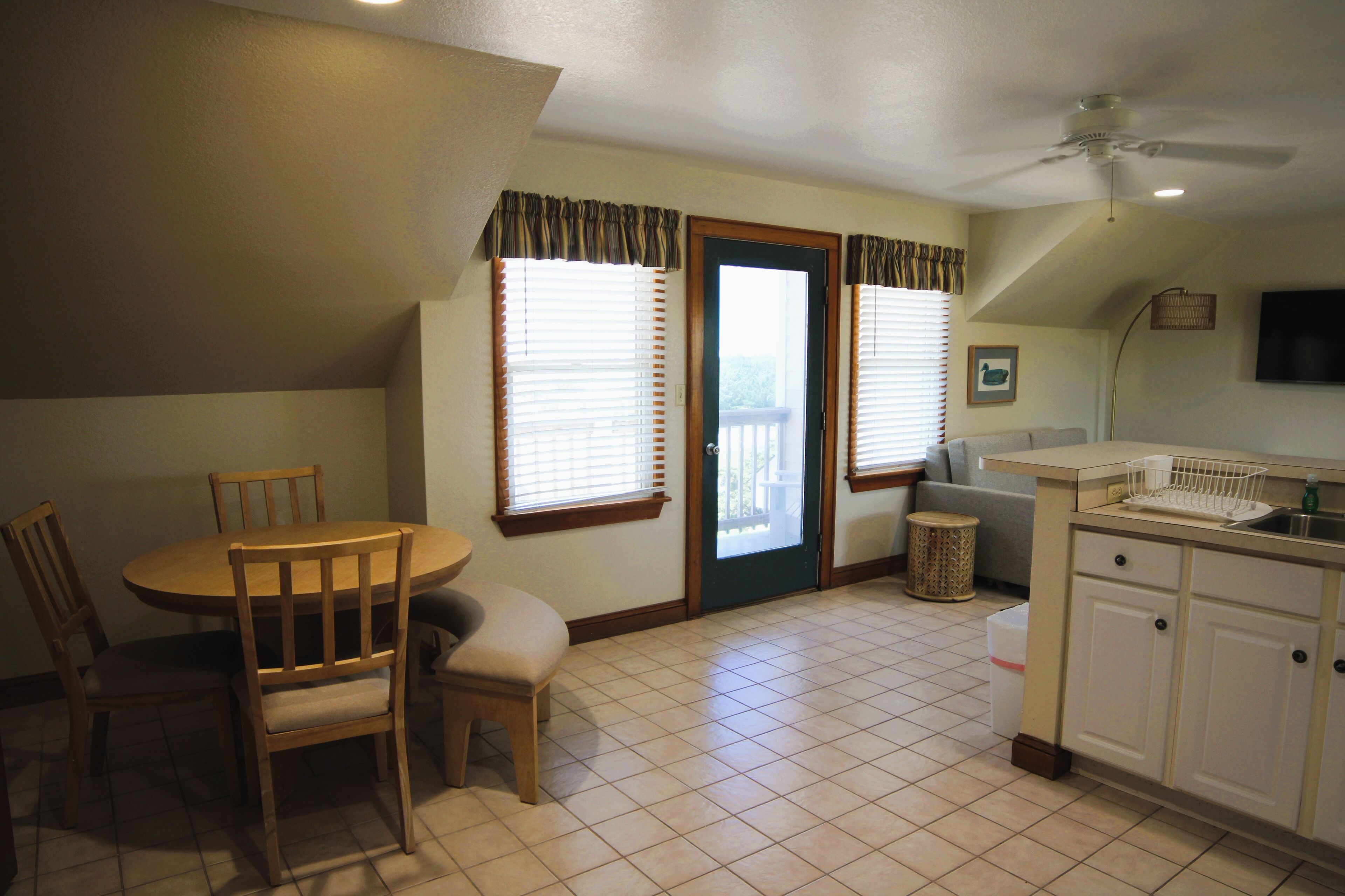 A kitchen with a dining table and chairs, a small trash can, and a ceiling fan.