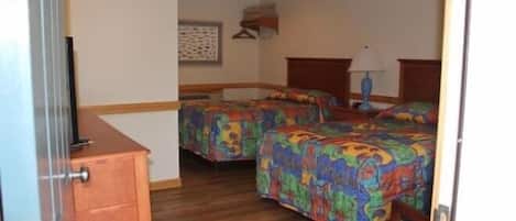 A hotel room with two beds, a wooden dresser, a ceiling fan, and a wall-mounted TV.