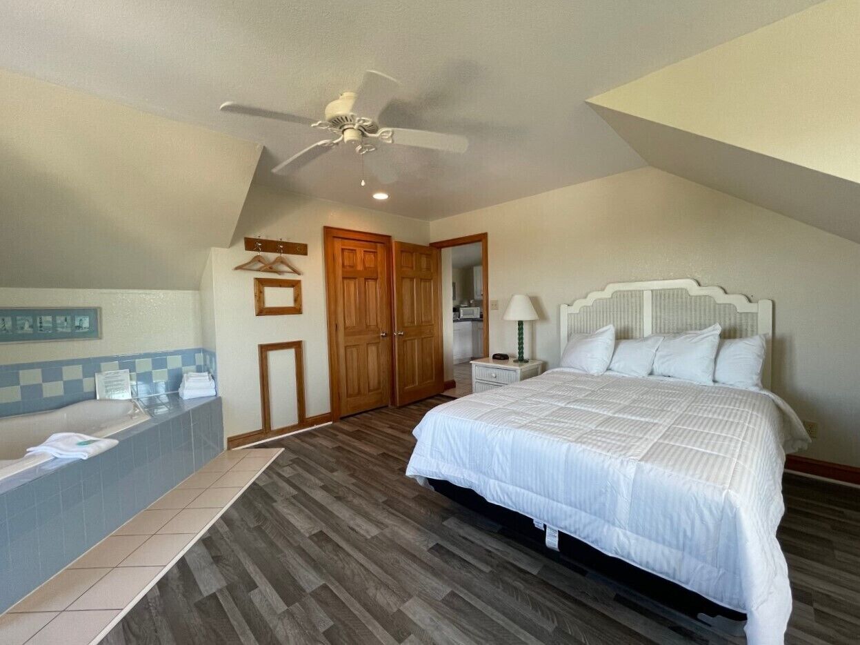Quarto com cama grande, ventilador de teto, banheira e piso de madeira.