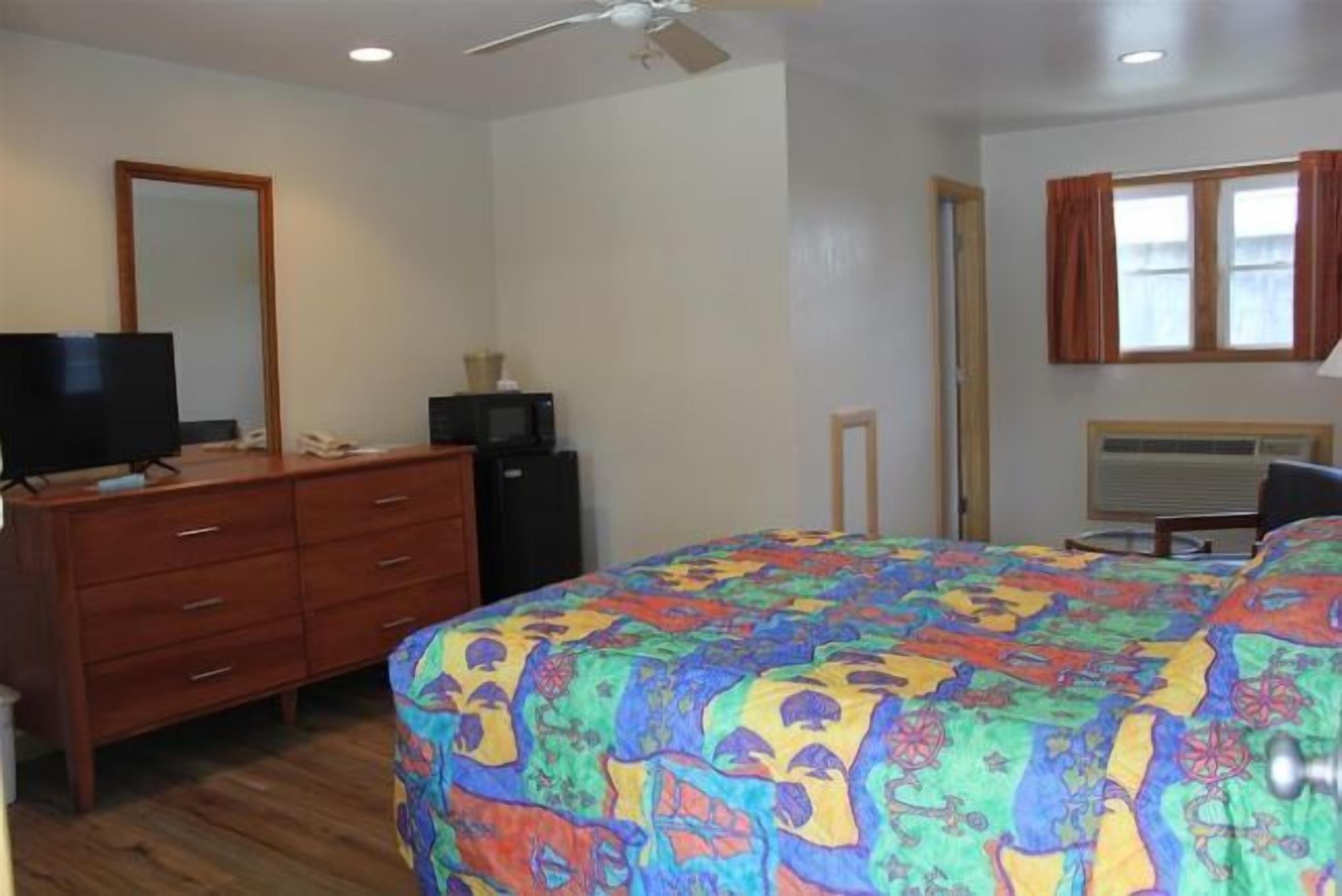 A bedroom with a bed, dresser, TV, and a ceiling fan.
