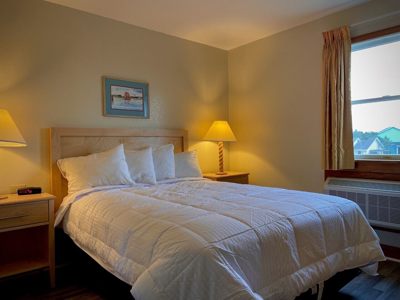 Habitación de hotel con cama, dos lámparas de noche, una mesita de noche, un cuadro enmarcado en la pared y una ventana con cortinas.
