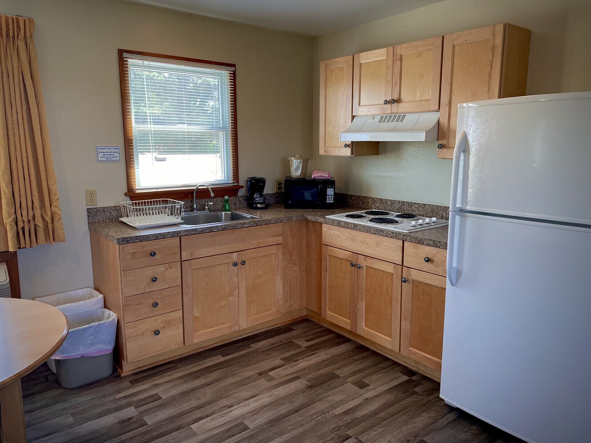 A compact kitchen with wooden cabinets, a white refrigerator, a built-in stove, and a window with blinds.