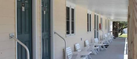A covered porch with white chairs and a handrail.