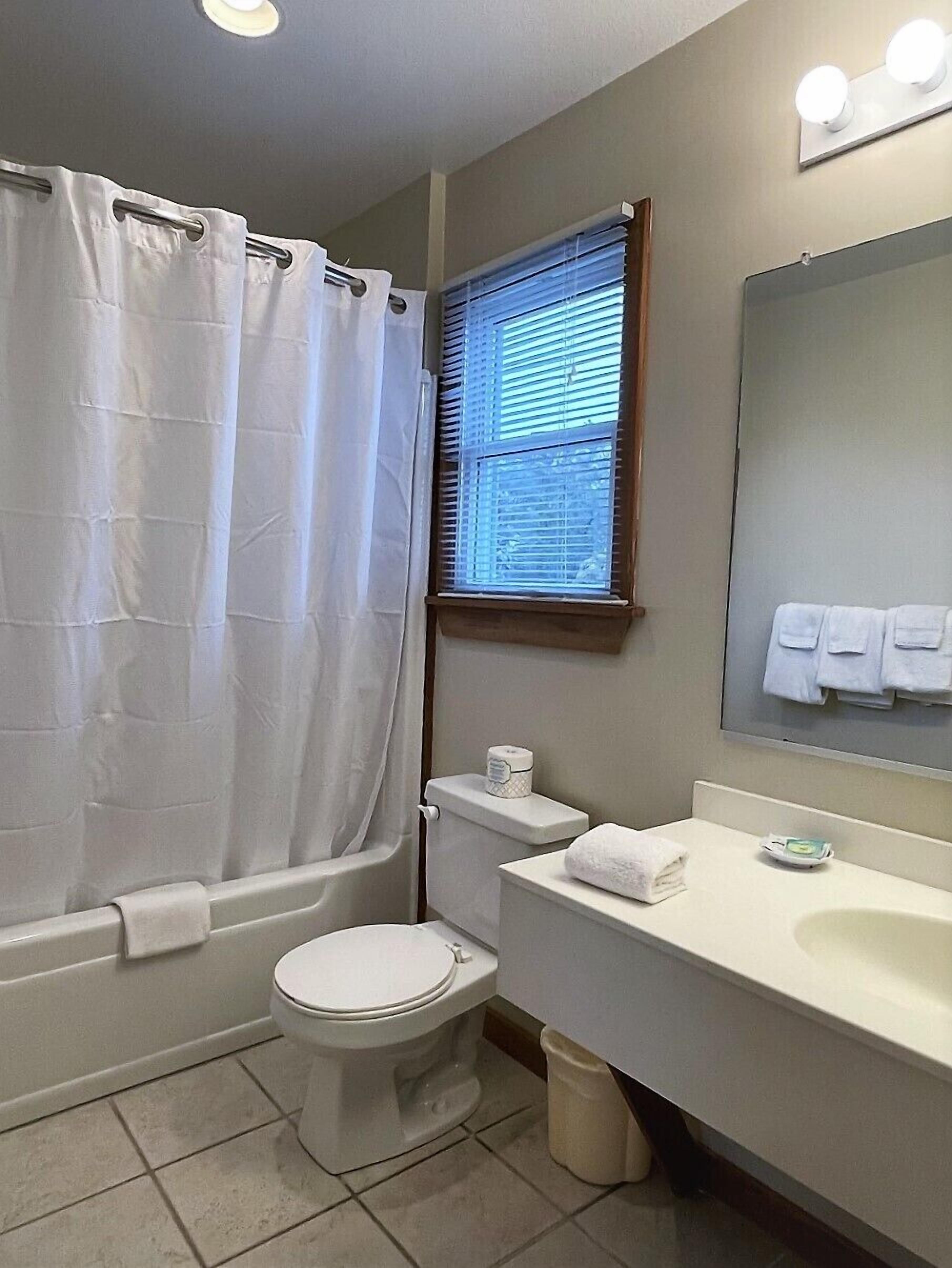 A bathroom with a bathtub, toilet, sink, and a window with blinds.