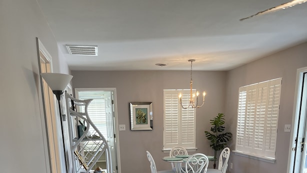 Una sala de estar con un sofá color beige, un comedor con sillas blancas, y una escalera que sube a otro nivel.