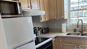 Una cocina con armarios de madera, microondas, refrigerador, tostadora y un lavaplatos.