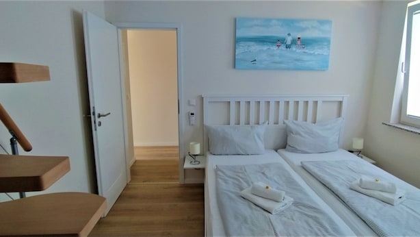 Ett hotellrum med två sängar, en målning som föreställer en strandscen, ett fönster och en trätrappa.