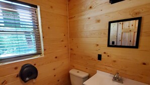 Un baño rústico en una cabaña de madera, con inodoro, lavamanos y ventana.