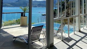 Un balcon moderne avec une porte vitrée, une piscine et une vue sur un lac et des montagnes.