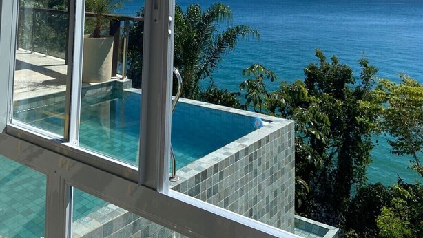 Un espace piscine moderne avec une eau d’un bleu cristallin, entouré d’une végétation luxuriante et offrant une vue panoramique sur la mer et les montagnes lointaines.