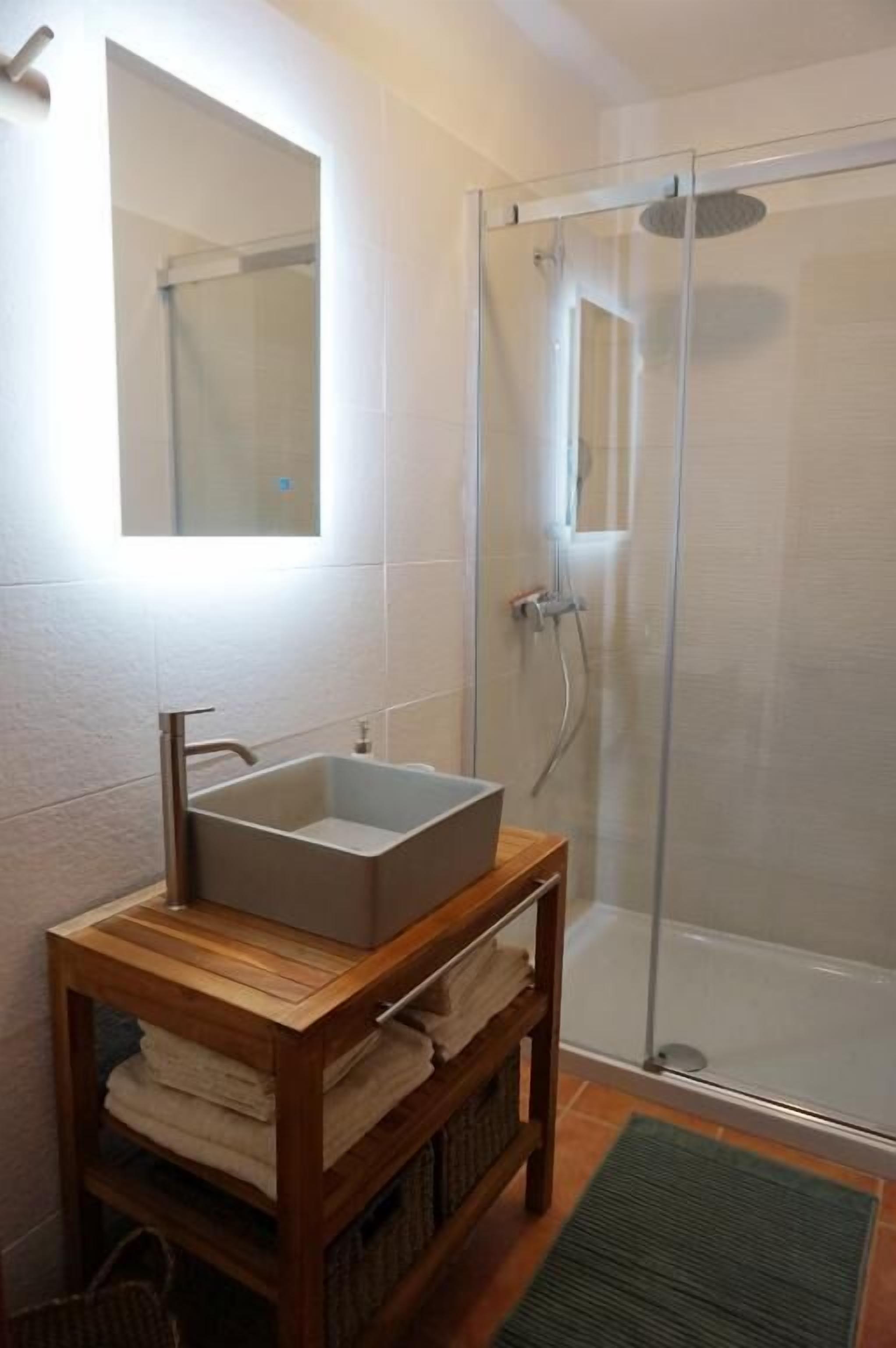 Une salle de bain avec une douche à parois de verre, un meuble-lavabo en bois et un miroir au-dessus du meuble-lavabo.