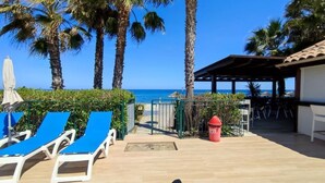 Ein Poolbereich mit blauen Liegestühlen, einer überdachten Sitzgruppe und Blick auf den Ozean.