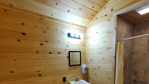 A wooden-paneled bathroom with a toilet, sink, and shower.