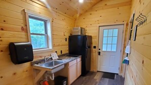 A compact wooden cabin with a kitchenette, including a sink, a refrigerator, and a window.