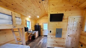 A cabin with two bunk beds, a kitchenette, a TV mounted on the wall, and a door.