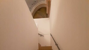 A staircase with wooden steps and a metal handrail, leading to a landing with a white wall and a blue patterned ceiling. - DUCHESS HOUSE (Varazze)
