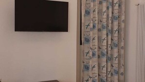 A room with a flat-screen TV mounted on the wall, a small wooden table, and a curtain with a bird pattern. - DUCHESS HOUSE (Varazze)