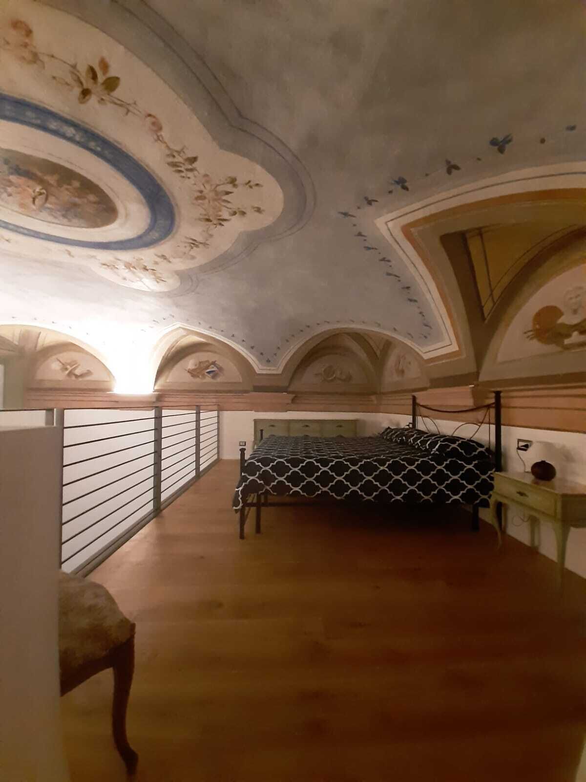 A bedroom with a bed, a chair, a desk, and a decorative ceiling.