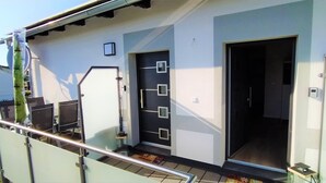 Een modern gebouw met een glazen balkon, een zwarte deur met geometrische patronen, en een klein terras.