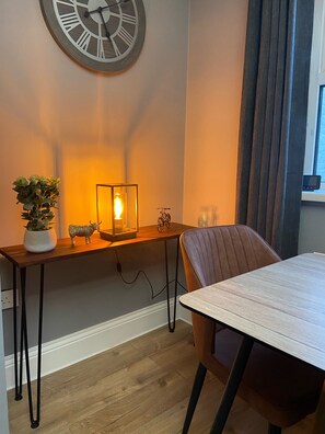 Un coin repas avec une table en bois, une chaise, une plante en pot, une horloge murale et une bougie allumée posée sur la table.