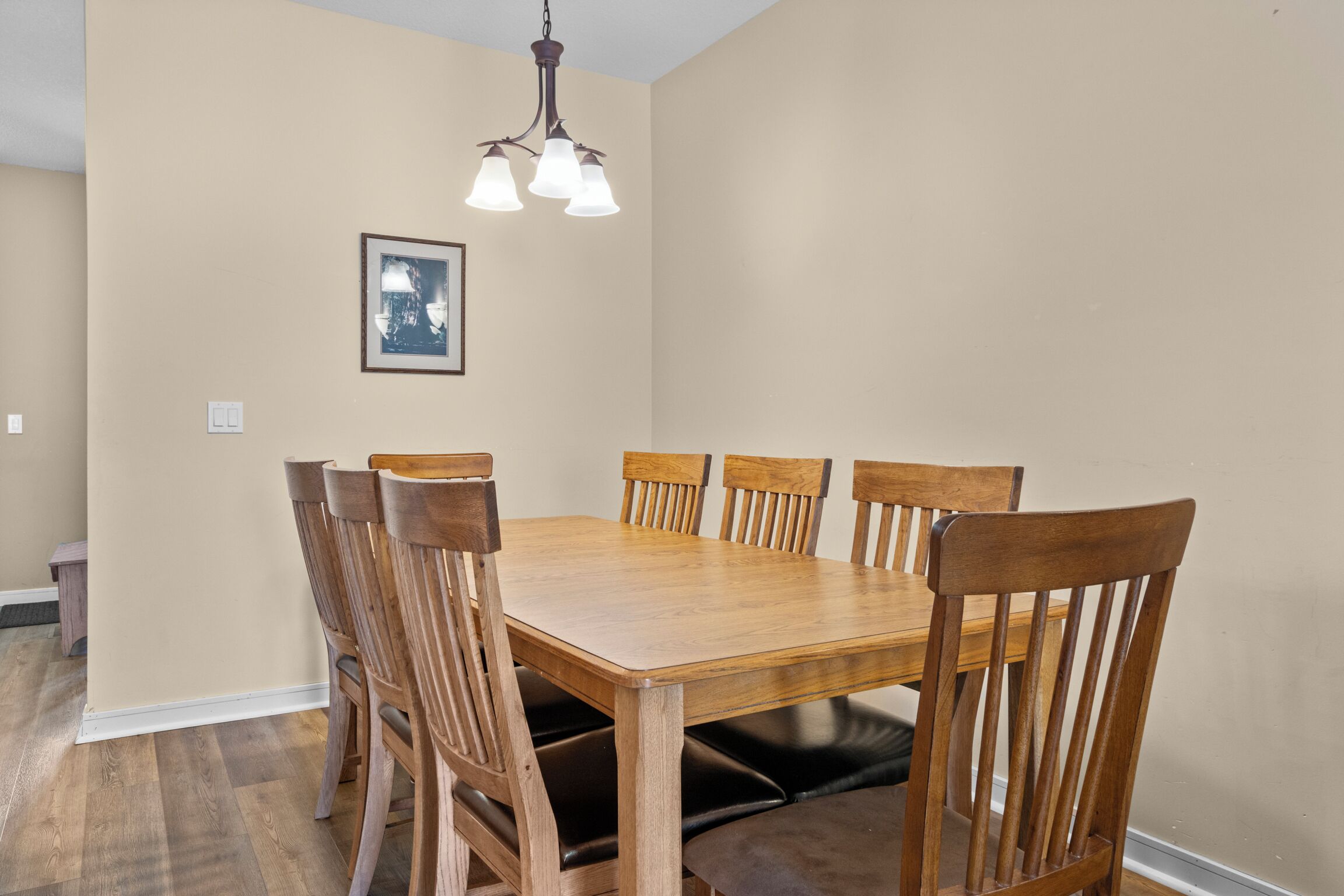 Une salle à manger avec une table et des chaises en bois, un lustre et un tableau encadré au mur.