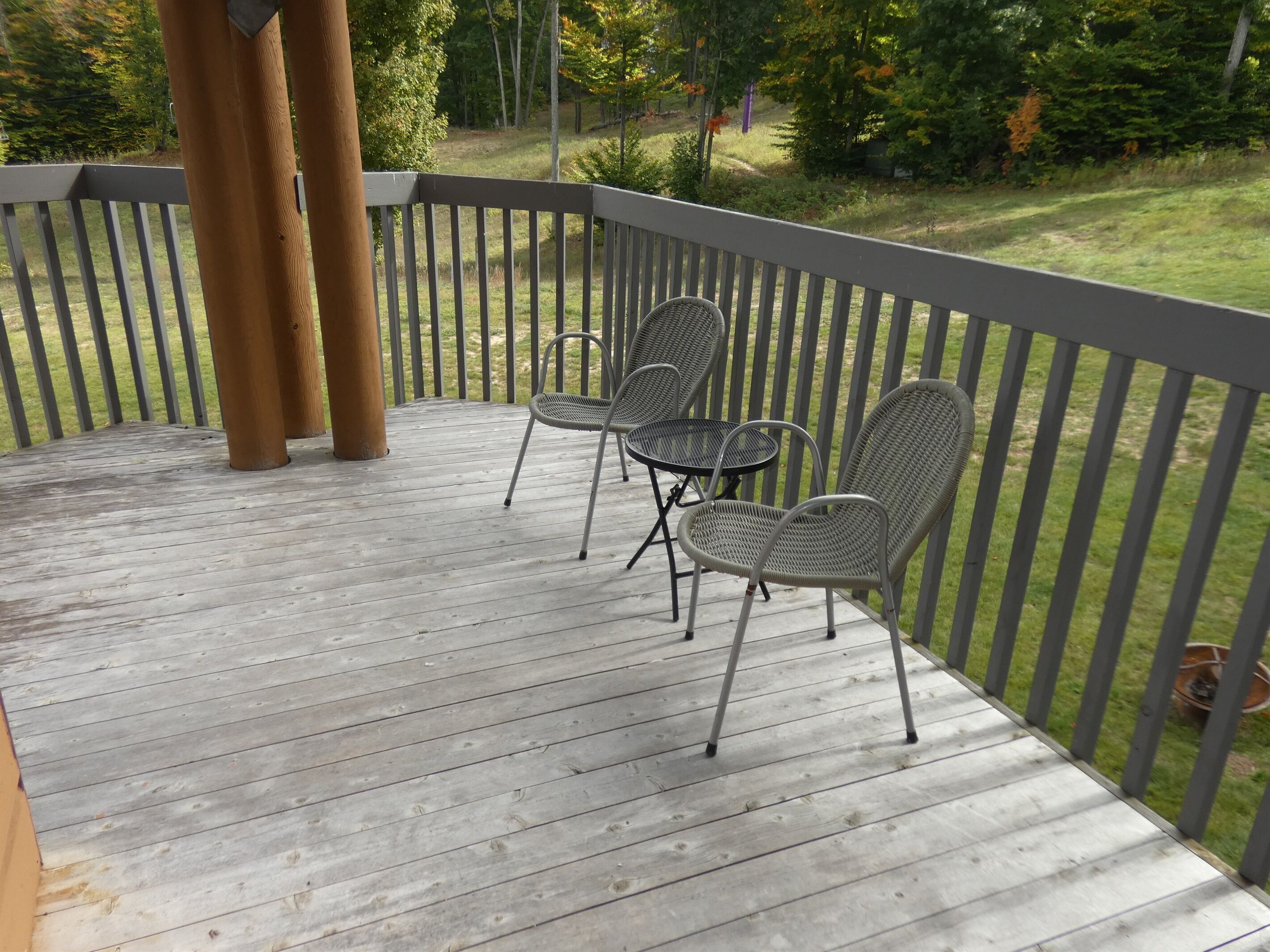 Een houten terras met metalen stoelen en een tafel, omringd door een grijze reling.