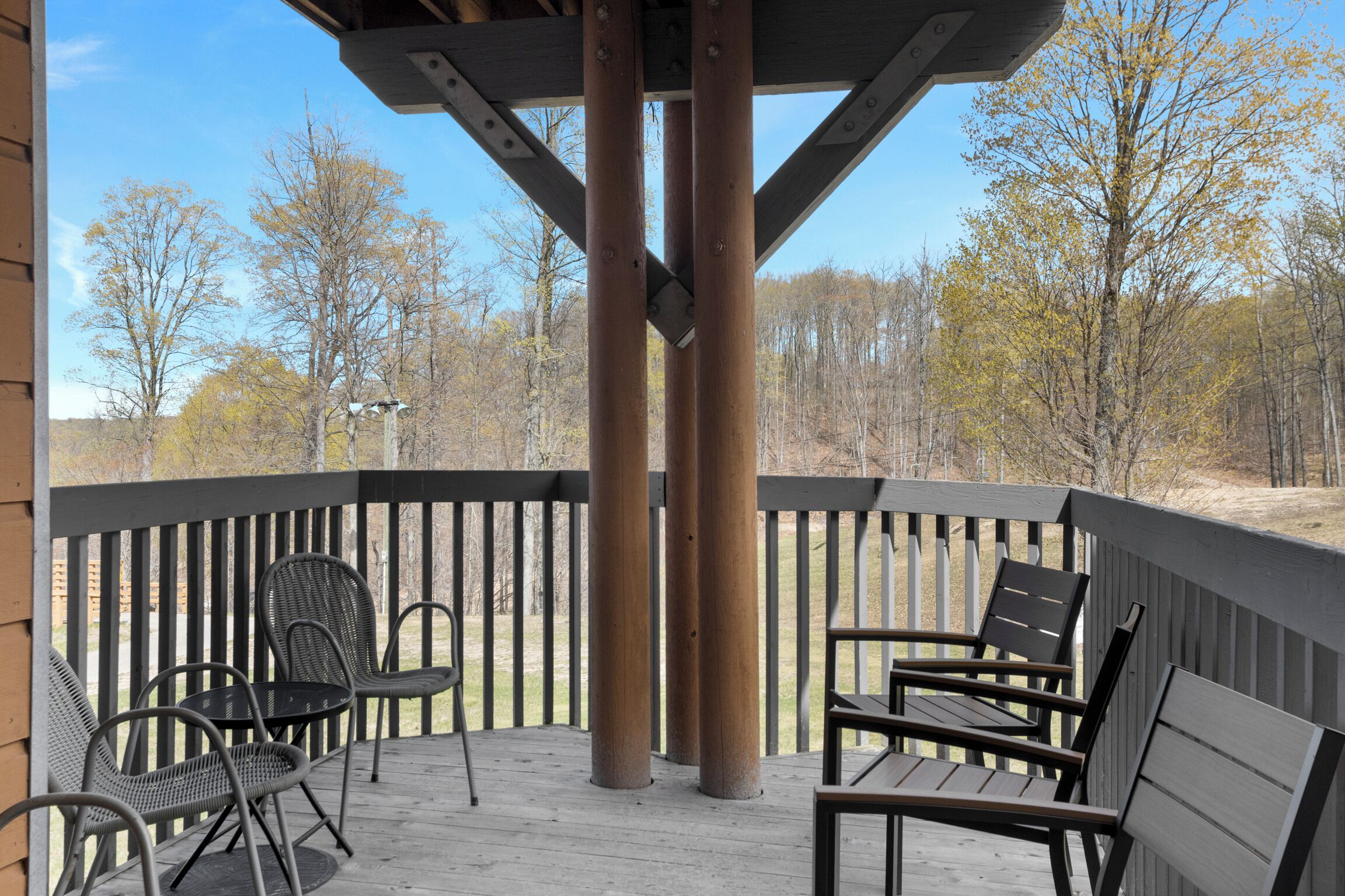 A covered outdoor seating area with metal chairs and a wooden table, surrounded by a wooden deck and metal columns.