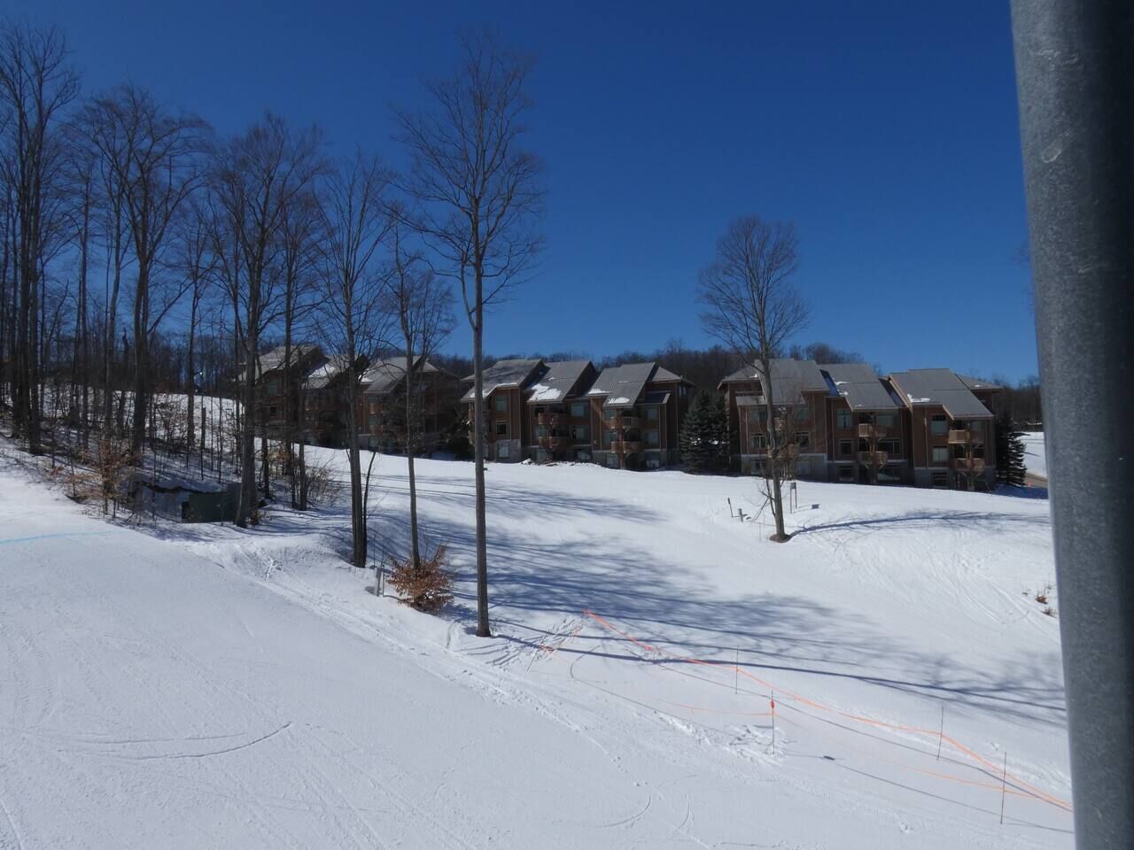 A snow-covered landscape with a row of multi-story buildings, likely a hotel or resort, with a clear blue sky.